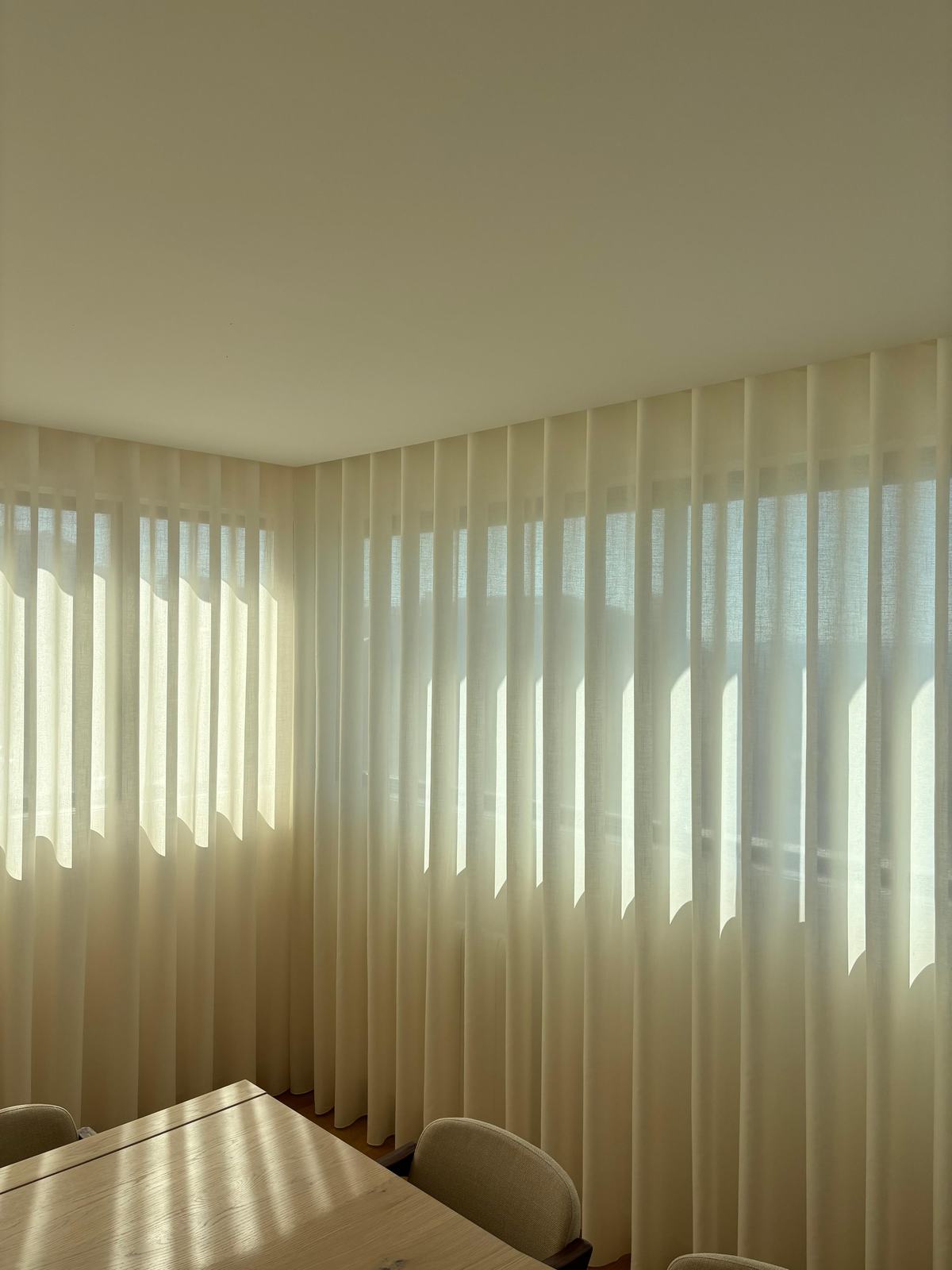 Cortinado de onda numa sala de jantar, com a luz do fim de tarde a filtrar pelo tecido