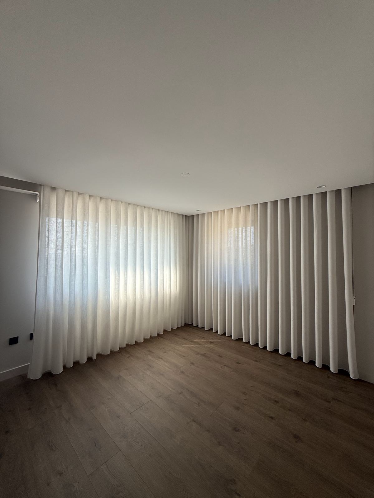 Divisão ainda vazia, com cortinados de onda em duas paredes e chão de madeira