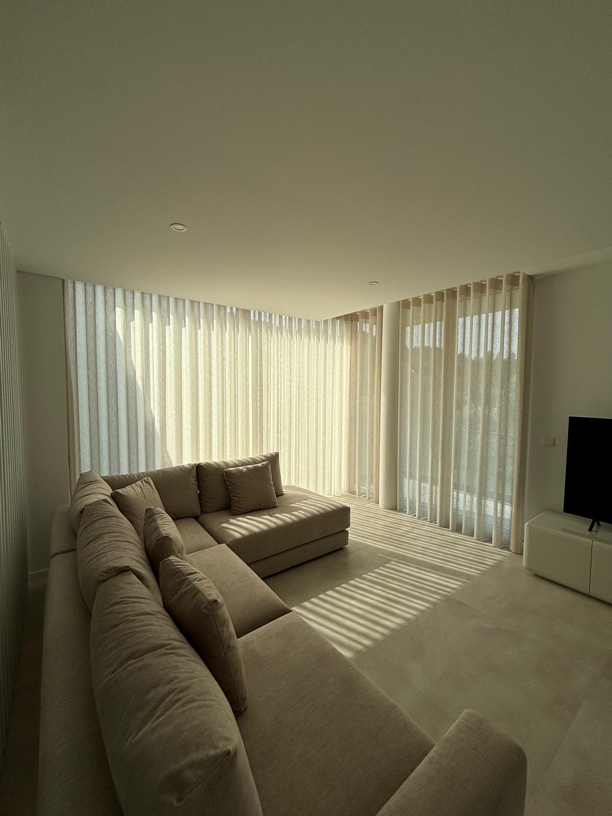 Sala de estar ampla com sofá em L, televisão e cortinados de onda