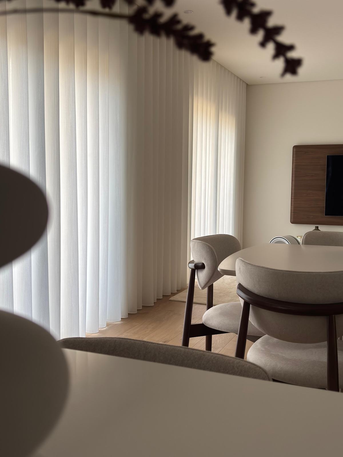 Sala de jantar clara com mesa redonda e cortinados de onda ao fundo